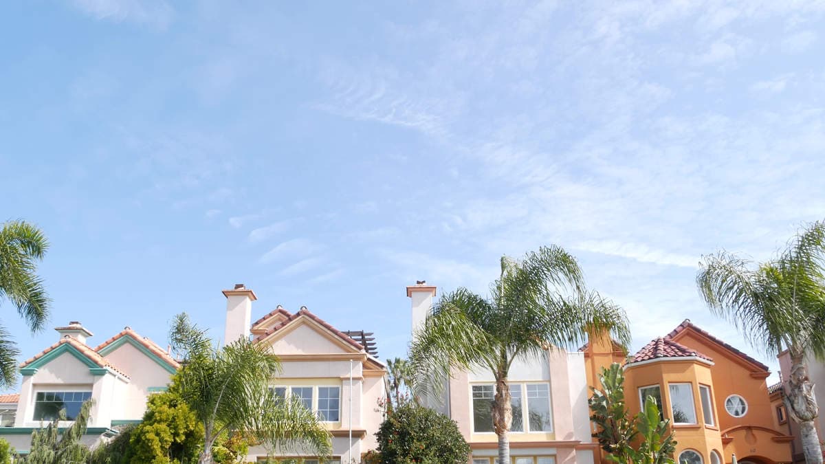 Eco-friendly exterior paint on California stucco homes with tile roofs and palm trees under a clear sky.
