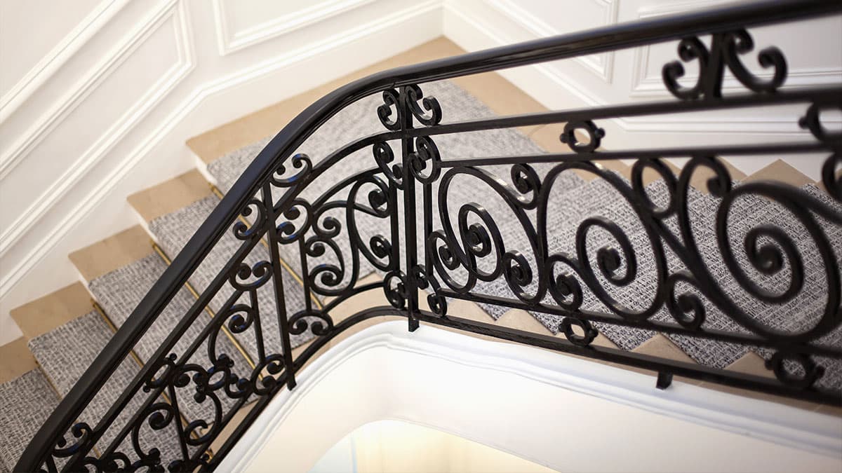 Black wrought-iron stair railing with curved scrollwork above carpeted steps and white trim.