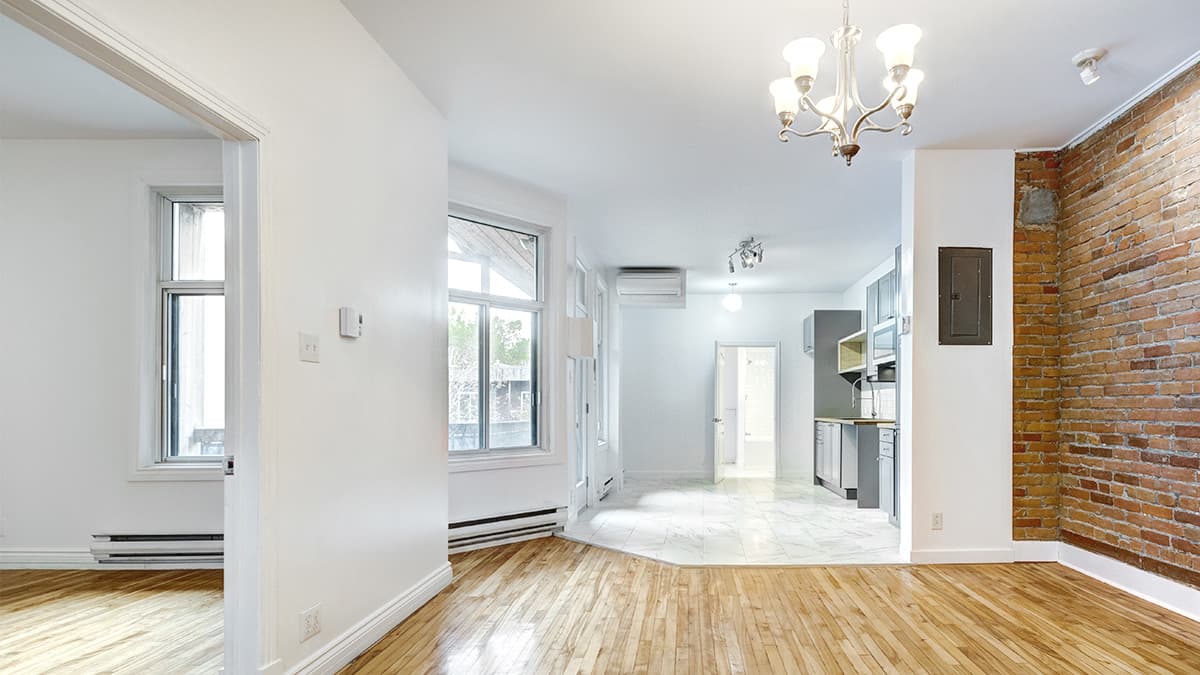 Empty home interior with white walls, hardwood floors, and an exposed brick accent wall prepared for a professional painting project