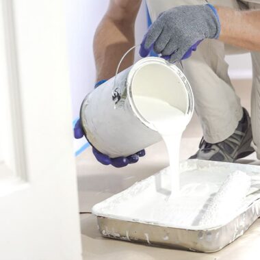 Professional painter pouring white paint into a tray before starting an interior painting